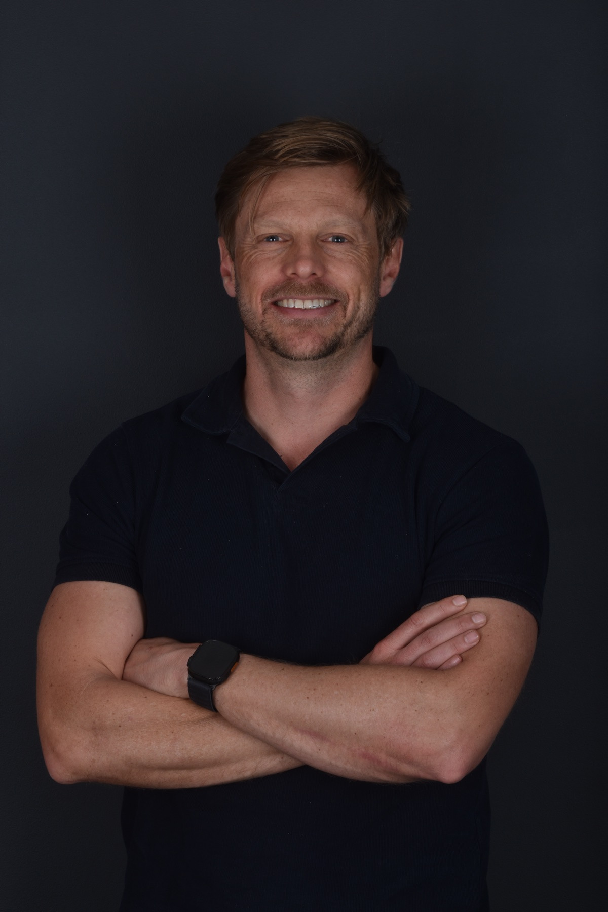 Cornu Laas, smiling, arms crossed, in a dark shirt against a dark backdrop