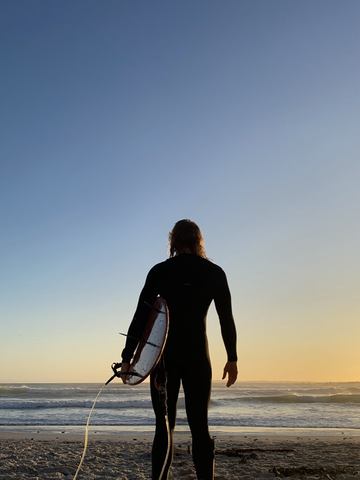 Cornu from behind at dawn, surfboard under his arm, facing the sea